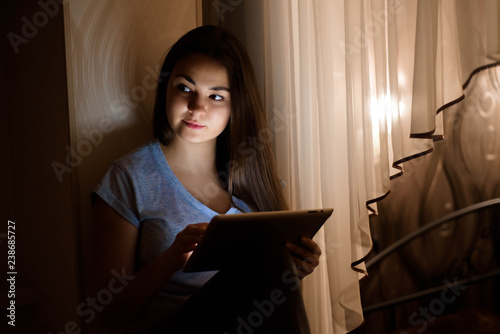 Young woman sitting by the window and using digital tablet at ho