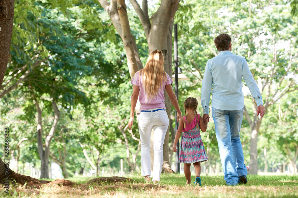 Rear view of mother and father holding hands of their daughter when walking in park Rear view of mother and father holding hands of their daughter when walking in park