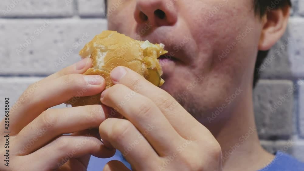 Man is eating a hamburger with relish and delight in cafe. Close-up hands and lips. Man is eating a hamburger with relish and delight in cafe. Close-up hands and lips.