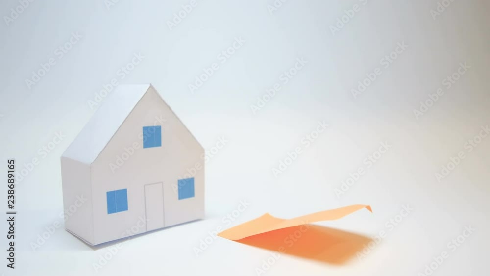hand rests next to a paper house purchase home symbol an orange post it