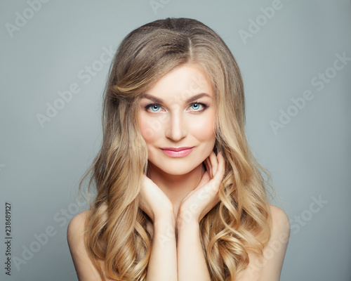 Beautiful blonde woman with long healthy curly hair and clear skin. Facial treatment, haircare and cosmetology