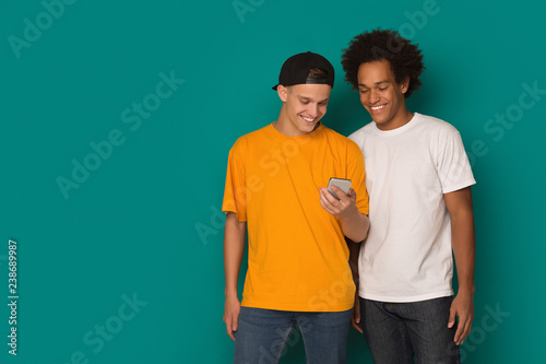 Two teenage guys using smatphone on blue background photo