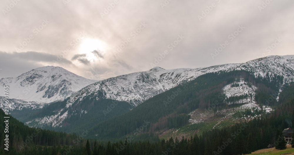 Awesome Mountains Ridge with Snow, Sun, Forest and Clouds driven by Strong Wind