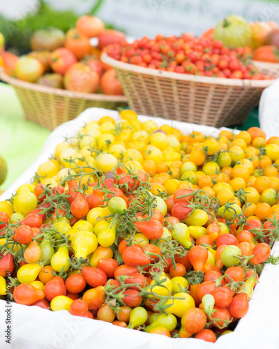 Detail on a market stall of fresh tomatoes, with focus on orange cherry tomatoes in the foreground. Organic food concept.