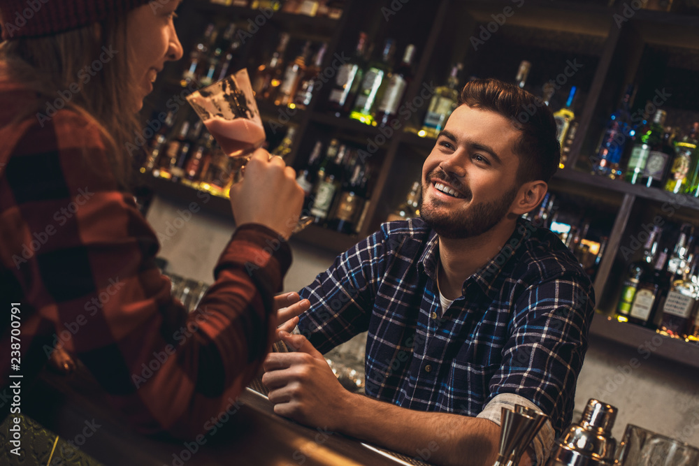 Young bartender leaning on bar counter talking with customer happy