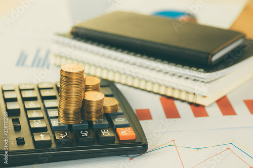 Coin stack and financial graph paper sheet with calculator on working table, business planning vision and finance analysis concept.