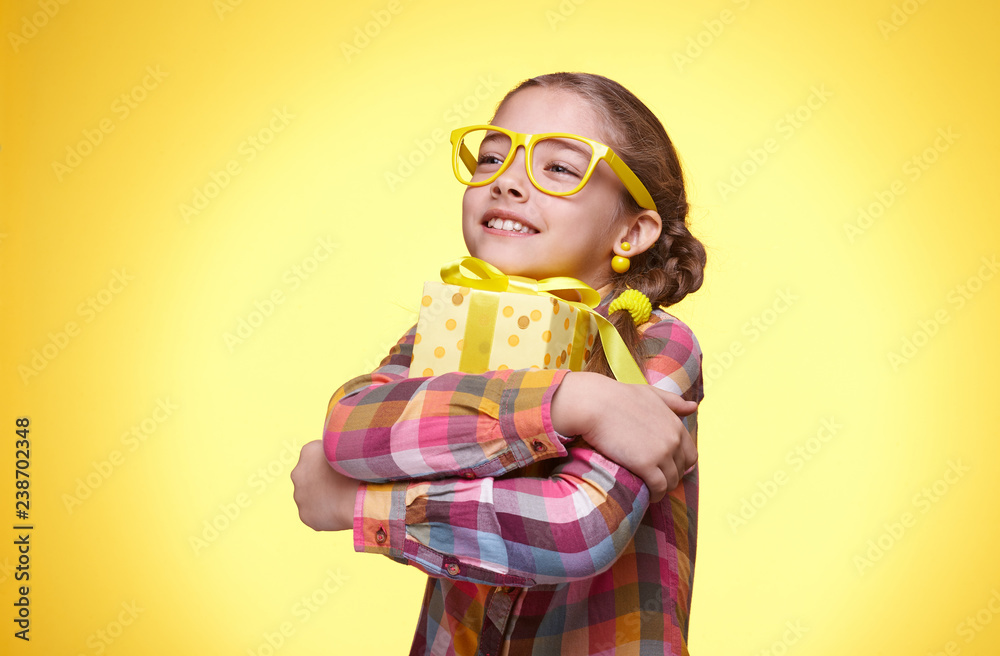 Happy teen girl with gift on yellow background