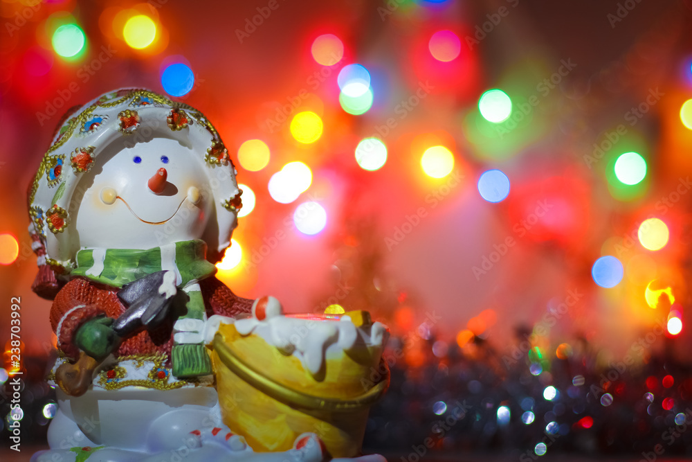 Snowman candlestick on the background of bright colored lights of garland and tinsel.