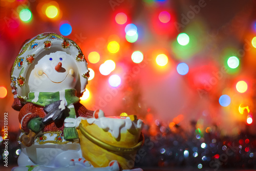 Snowman candlestick on the background of bright colored lights of garland and tinsel.