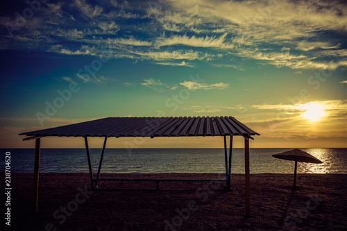 Fototapeta Naklejka Na Ścianę i Meble -  Canopy and old metal umbrella on an empty sandy beach at sunset.