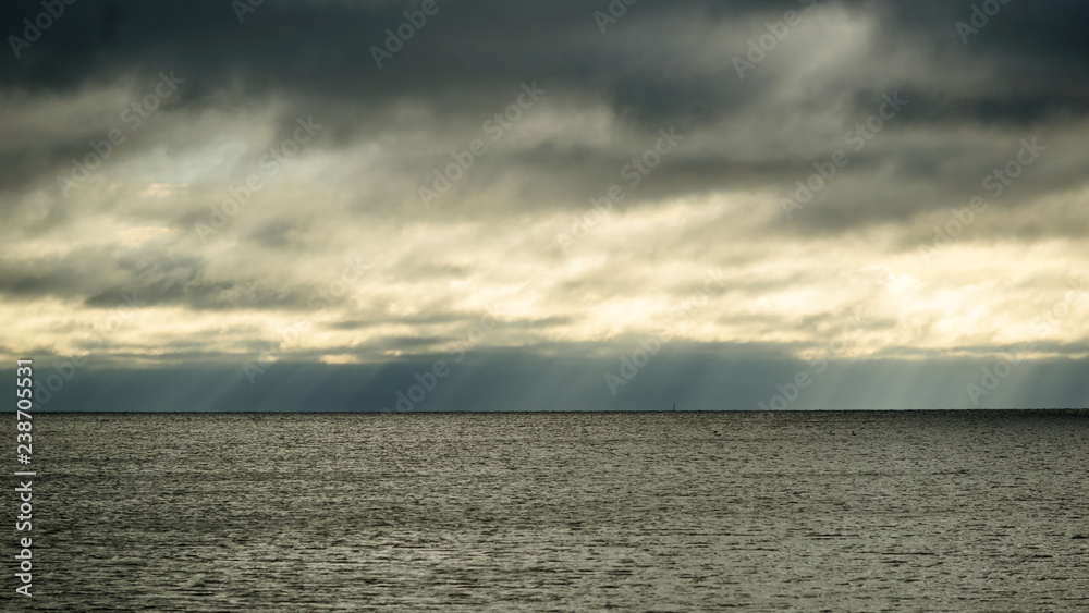 Rainclouds dispersing, letting subtle rays of sunshine through over a dark and sinister horizon.