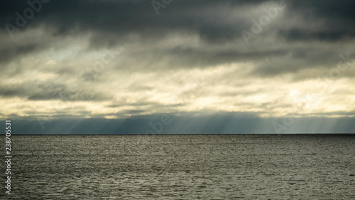 Photography Rainclouds dispersing, letting subtle rays of sunshine through over a dark and sinister horizon