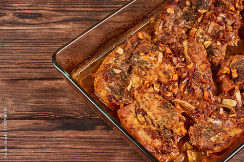 Juicy baked meat in a glass cookware on a brown wooden bakground