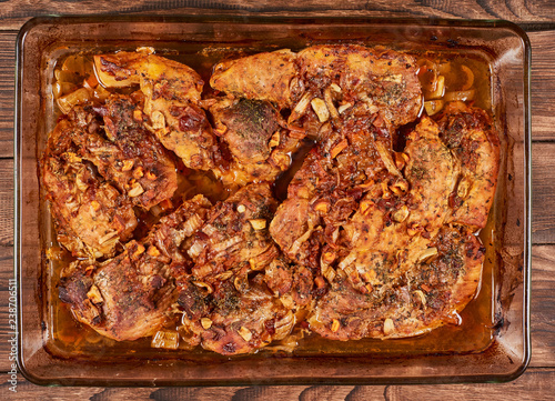 Juicy baked meat in a glass cookware on a brown wooden bakground, falt lay photo