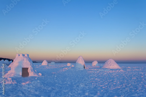 The camp consists of several snowy houses called an igloo in the rays of the setting sun.