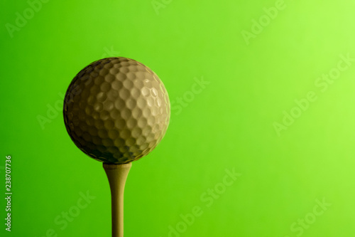 Close-up the shady side of a golf ball on a tee. Copy space. Bright green salad background.