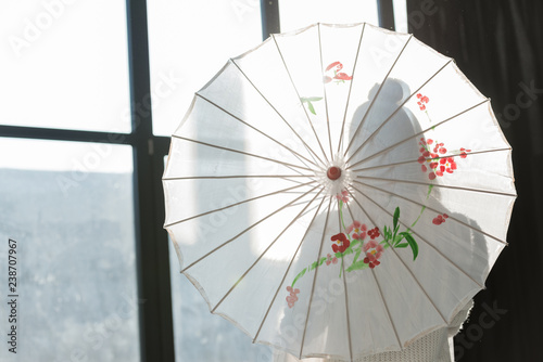 silhouette of woman standing with paper umbrella near window