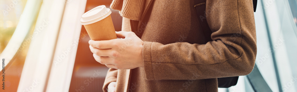 Fototapeta premium cropped view of man in warm clothing standing on escalator and holding disposable cup
