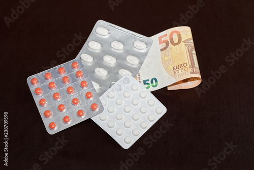 Pills in blister packaging and 50 Euro banknote on dark background