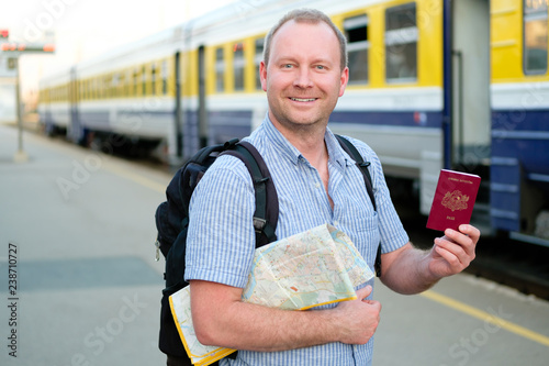 Happy Man with smile standing on the platform of the railway station with travel map and shows passport to camera. Train travel concept photo