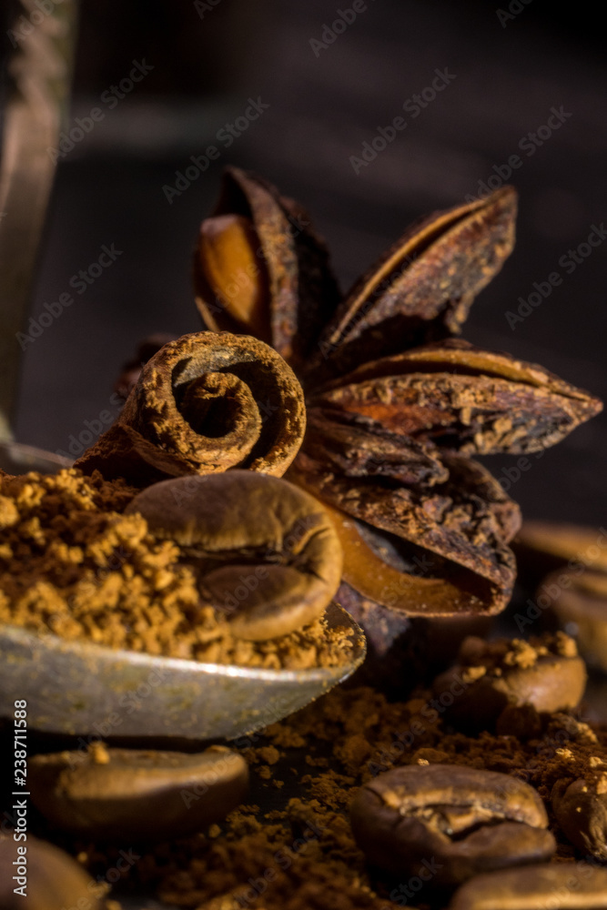 Stick of cinnamon and oriental spices, aniseed cocoa, with a vintage spoon of ground coffee and unroasted grains on a dark background. free space for your text. Close-up macro image.