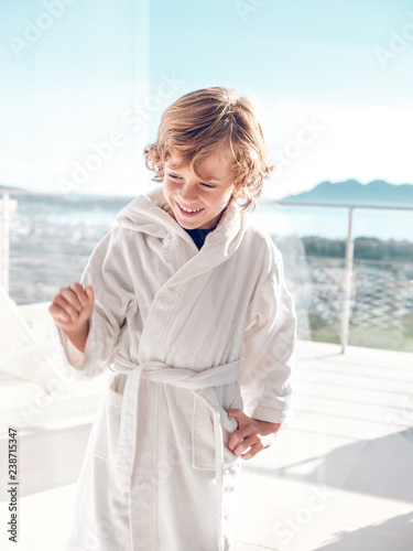 Cheerful boy in bathrobe standing on terrace