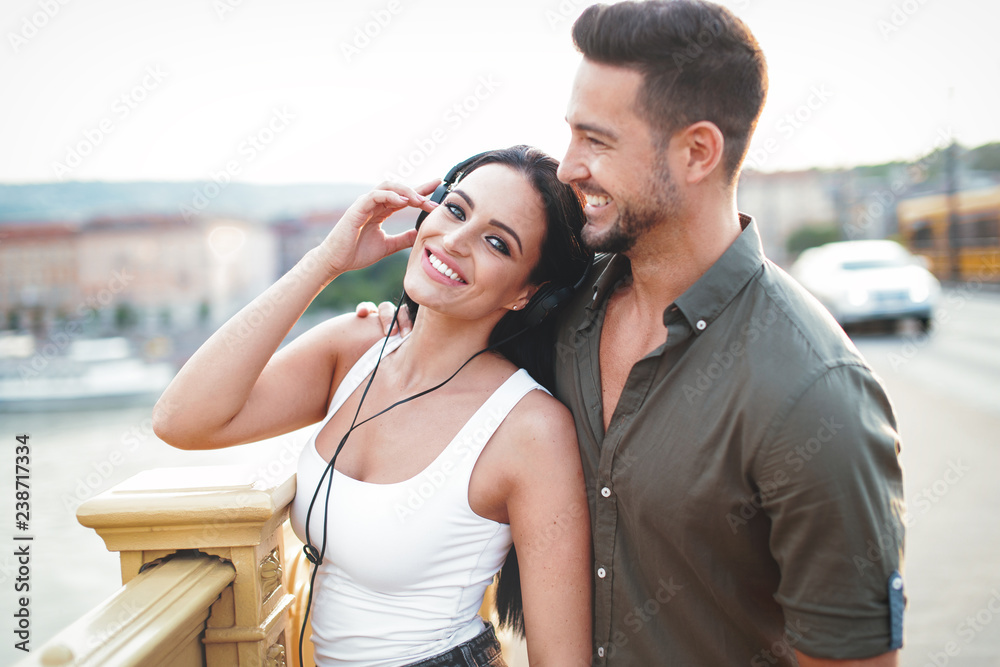 Happy young couple listening music in city by headphones at outdoors