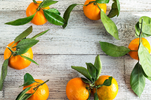 Border of orange tangerines with green leaves on white wooden background. Top view and copy space.