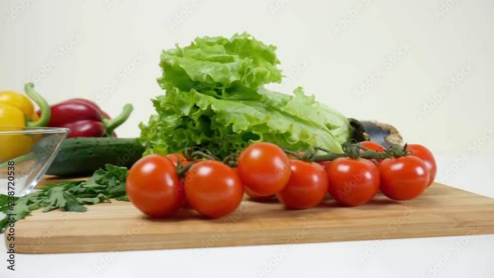 Healthy food. Vegetarian food. Ingredients for the salad on the table. Lettuce, cherry tomatoes, cucumber, red and yellow peppers, parsley. Glass bowl for salad. The camera moves from right to left. Healthy food. Vegetarian food. Ingredients for the salad on the table. Lettuce, cherry tomatoes, cucumber, red and yellow peppers, parsley. Glass bowl for salad. The camera moves from right to left.