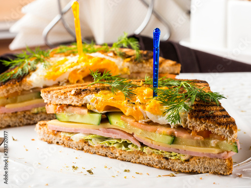 Club sandwich with egg, cucumber, tomato, ham. Two club sandwiches on white plate on dark brown wooden table in restaurant photo