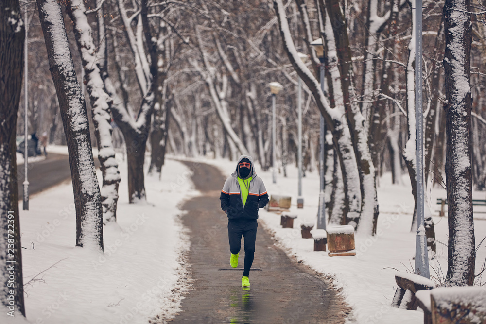 Man jogging in a cold winter snowy day outdoors.