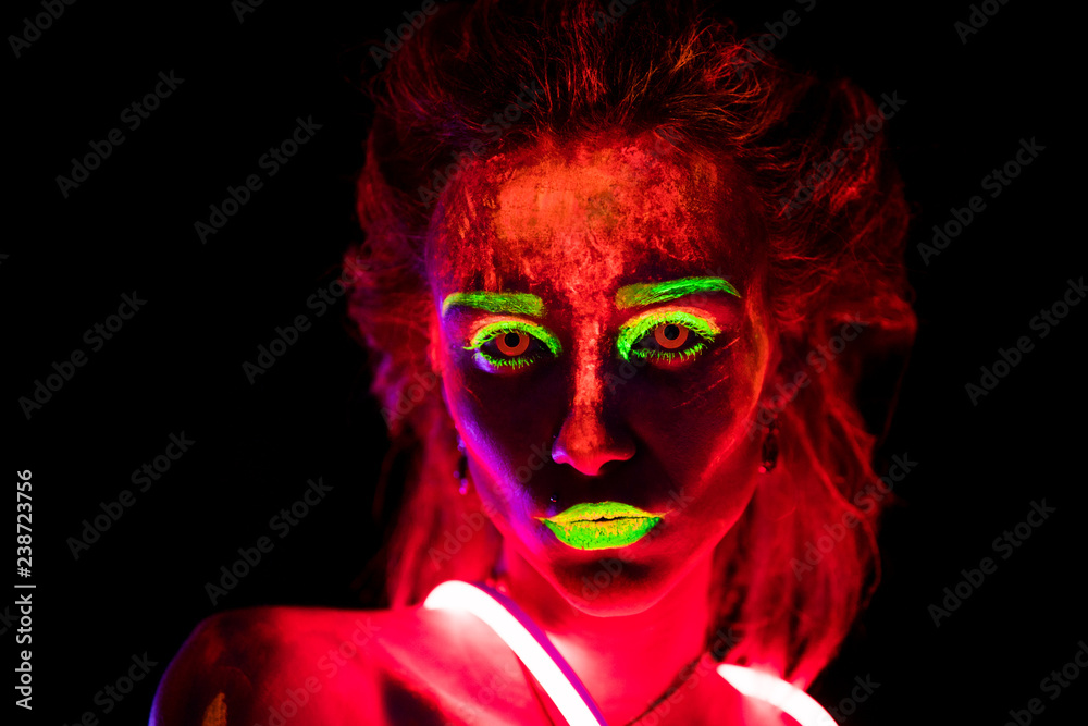 Portrait of a beautiful young sexy girl in neon lent with ultraviolet paint on her body. Pretty woman with glowing bodyart in black lamp light