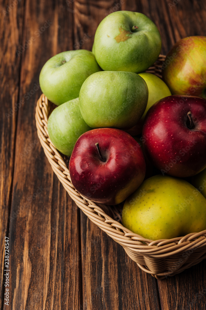 wicker basket with tasty multicolored apples on wooden table