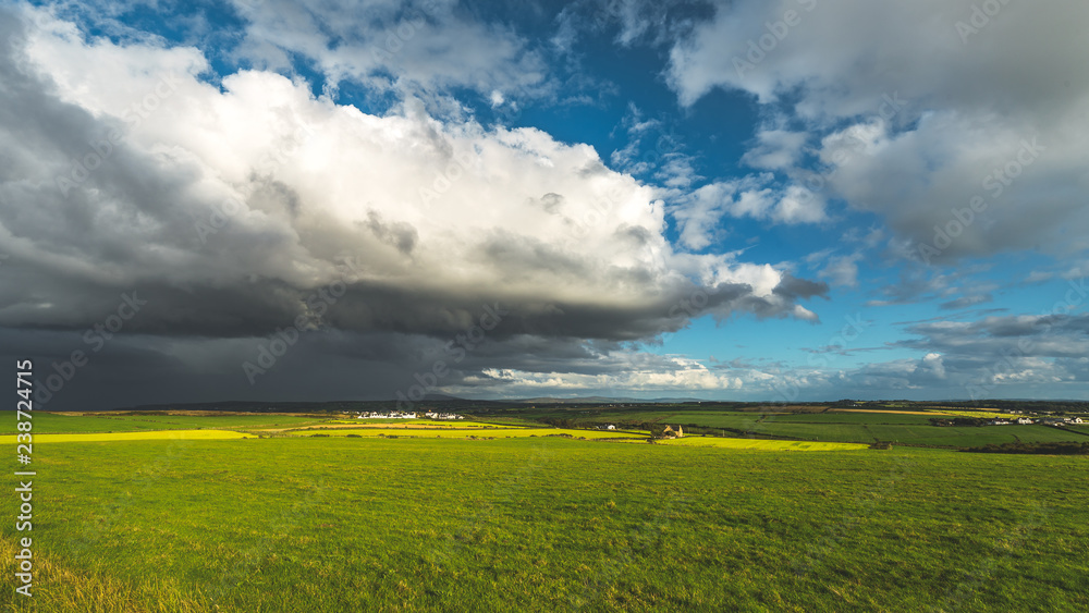 Fototapeta premium Heavy rainy clouds over the Northern Ireland field. Stunning countryside landscape. Green grass covered meadow under the colorful sky before the rain. Panoramic view of the wild virgin nature.