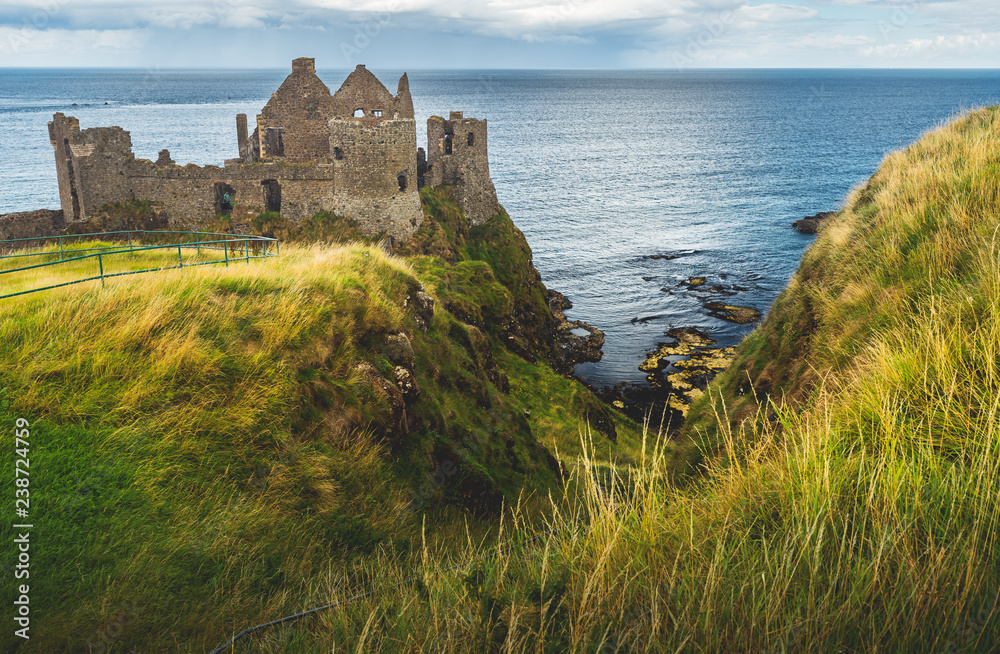 Dunluce castle on the green covered cliff. Irish shoreline. Overwhelming Northern Ireland landscape. Ancient now-ruined Medieval building with the ocean view. Famous archeological and touristic site.