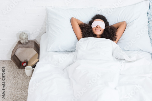 high angle view of african american girl with eyes covered by sleeping blindfold in bed during morning time at home