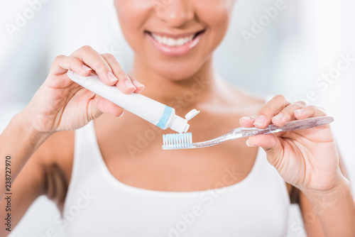 partial view of young woman putting toothpaste on toothbrush
