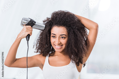 smiling curly african american girl drying hair at home