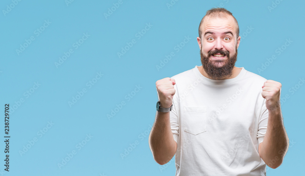Fototapeta premium Young caucasian hipster man wearing casual t-shirt over isolated background celebrating surprised and amazed for success with arms raised and open eyes. Winner concept.
