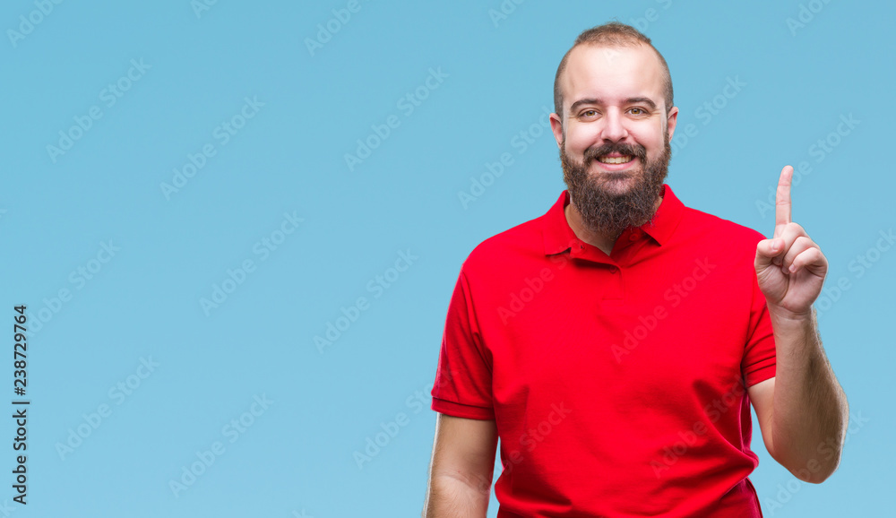 Young caucasian hipster man wearing red shirt over isolated background showing and pointing up with finger number one while smiling confident and happy. Young caucasian hipster man wearing red shirt over isolated background showing and pointing up with finger number one while smiling confident and happy.