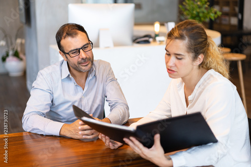 Serious businesswoman showing papers to mid adult executive. Mid adult businessman wearing glasses having meeting having meeting with young partner or colleague. Meeting concept