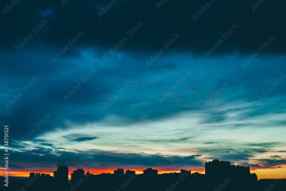 Fototapeta Cityscape with wonderful varicolored vivid dawn. Amazing dramatic multicolored cloudy sky above dark silhouettes of city buildings. Atmospheric background of sunrise in overcast weather. Copy space.