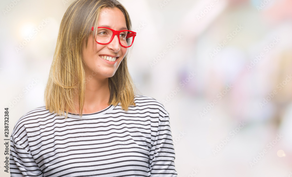 Young beautiful woman wearing glasses over isolated background looking away to side with smile on face, natural expression. Laughing confident. Young beautiful woman wearing glasses over isolated background looking away to side with smile on face, natural expression. Laughing confident.