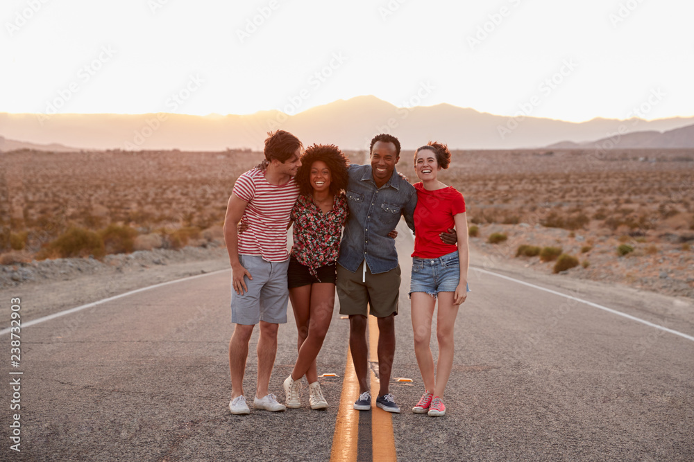 Four friends standing on a desert highway looking to camera Four friends standing on a desert highway looking to camera