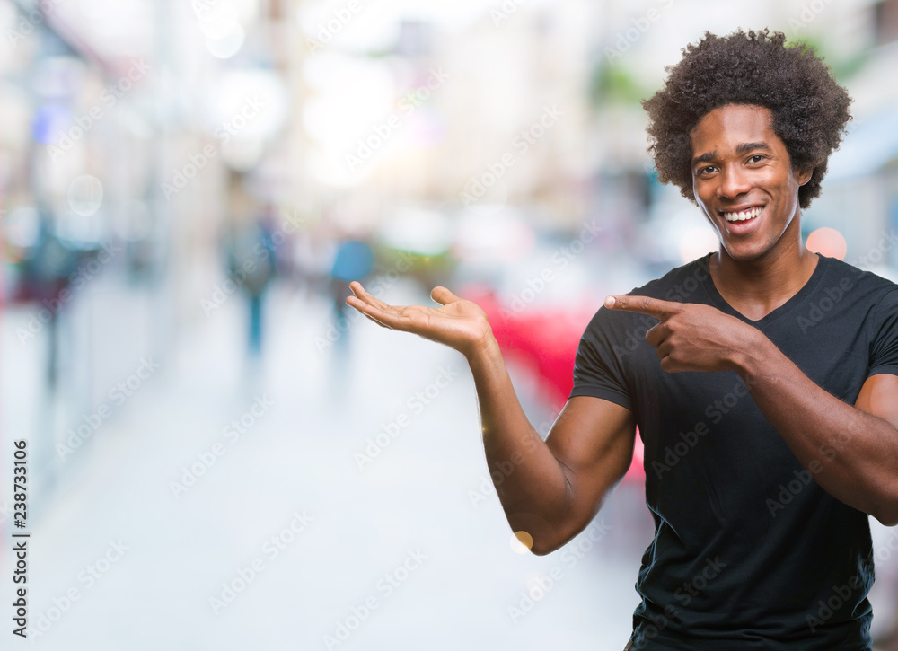Afro american man over isolated background amazed and smiling to the camera while presenting with hand and pointing with finger. Afro american man over isolated background amazed and smiling to the camera while presenting with hand and pointing with finger.