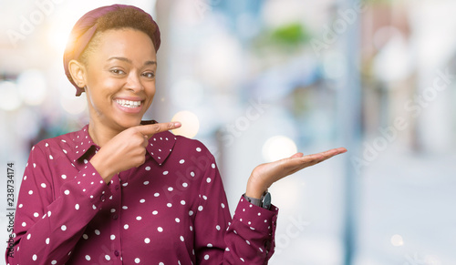 Beautiful young african american woman wearing head scarf over isolated background amazed and smiling to the camera while presenting with hand and pointing with finger.