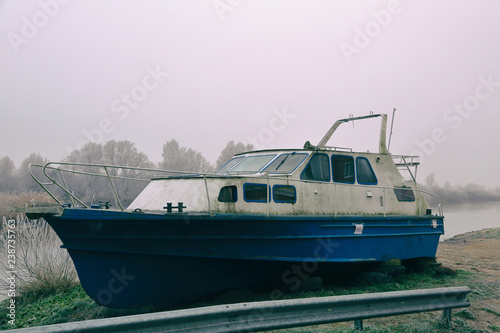 White-blue abandoned rusty boat on the banks of a misty river © ironstuffy