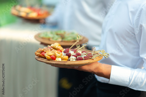 Catering - food, plate and hand. Waiters carrying plates with sweets, croissants and fruits at a wedding