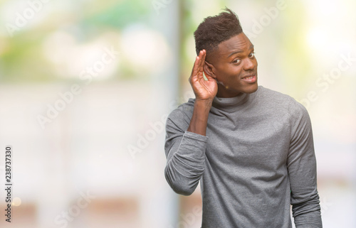 Young african american man over isolated background smiling with hand over ear listening an hearing to rumor or gossip. Deafness concept.