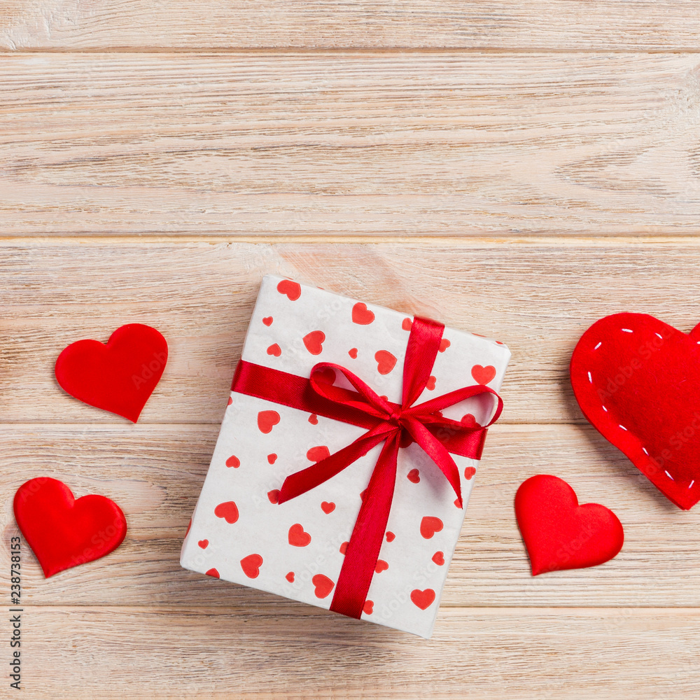 Valentine or other holiday handmade present in paper with red hearts and gifts box in holiday wrapper. Present box of gift on orange wooden table top view with copy space, empty space for design Valentine or other holiday handmade present in paper with red hearts and gifts box in holiday wrapper. Present box of gift on orange wooden table top view with copy space, empty space for design
